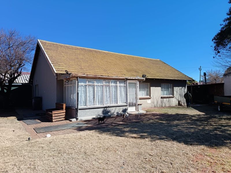 Rear view of the house featuring a tiled roof, an enclosed sunroom, and a paved patio area leading to the garden.