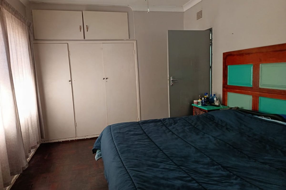 A bedroom featuring built-in cupboards, wooden flooring, and a ceiling fan, offering a functional space with potential for cosmetic updates.