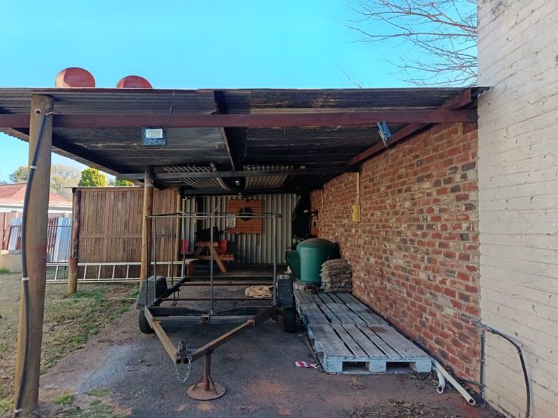 A covered outdoor patio area featuring a corrugated iron roof, exposed brick wall, and steel structural supports, offering potential for an outdoor entertainment space.