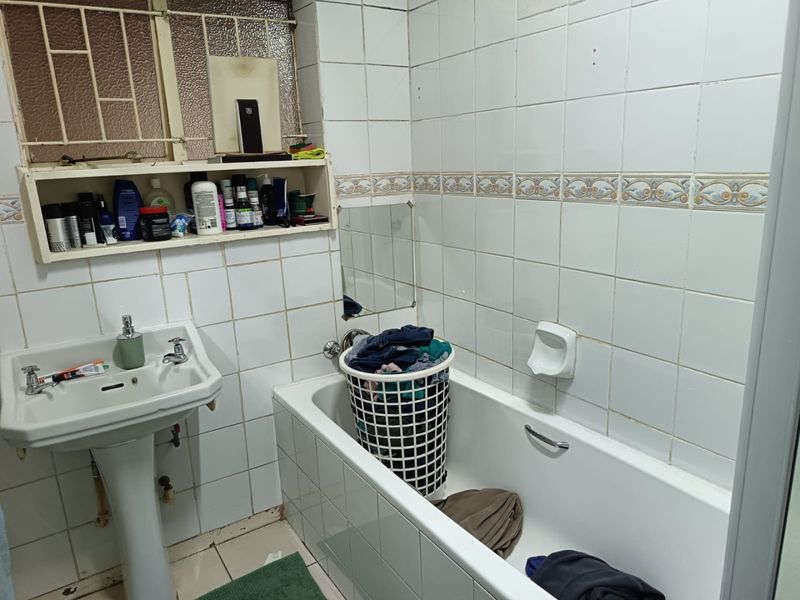 A dated bathroom featuring a pedestal basin, bathtub, and tiled walls with built-in shelving, requiring cosmetic updates to improve its overall condition.