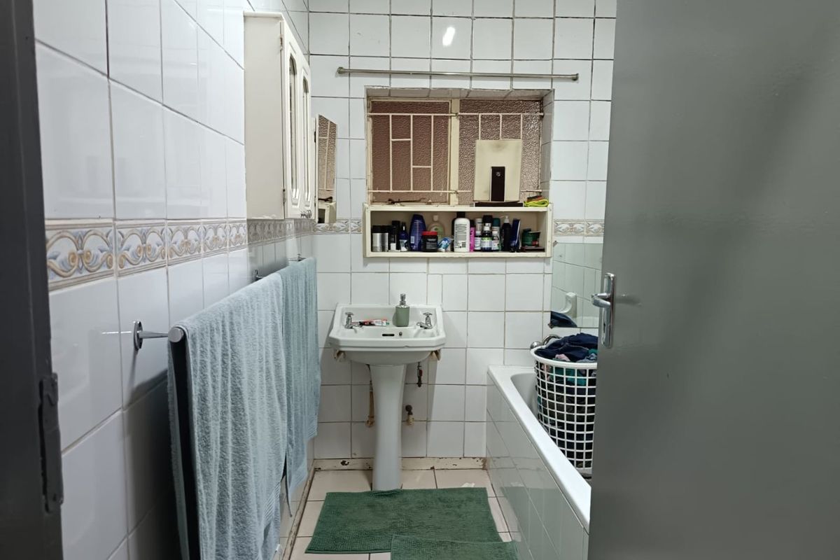 A functional bathroom featuring a pedestal basin, bathtub, and full-height wall tiling, requiring cosmetic updates to modernize the space.