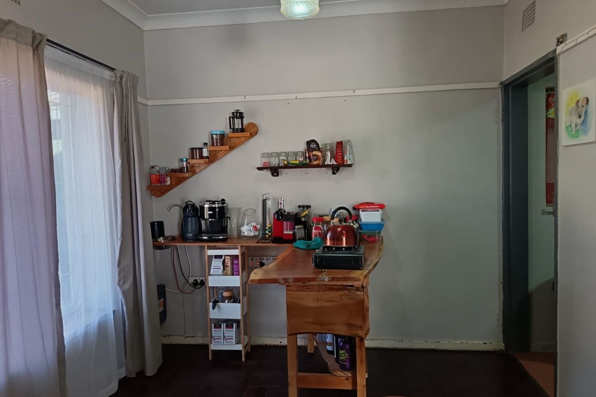 A small kitchen area featuring timber flooring, cove cornicing, and wall-mounted shelving, currently utilized as a coffee and prep station.