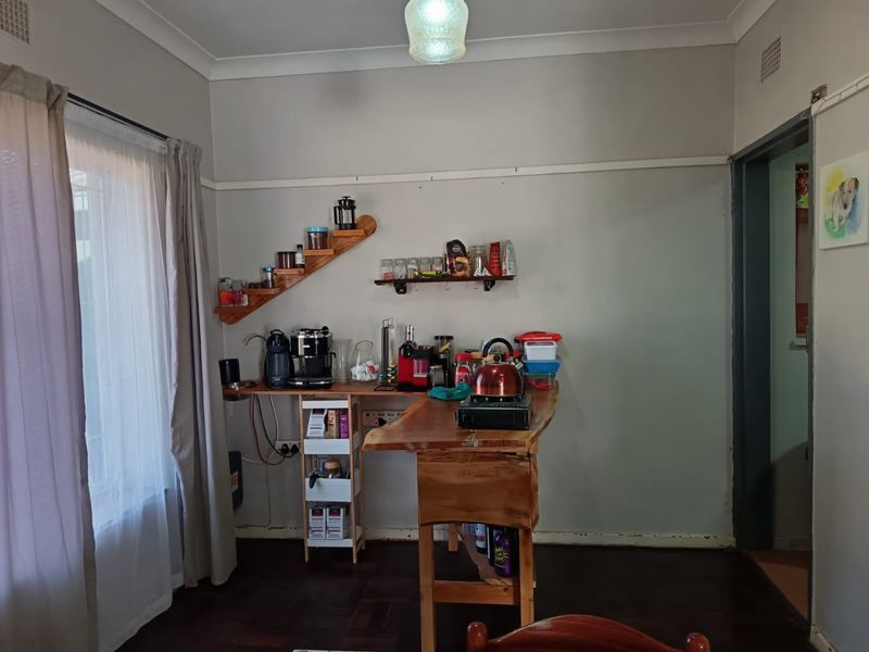 A small kitchen area featuring timber flooring, cove cornicing, and wall-mounted shelving, currently utilized as a coffee and prep station.