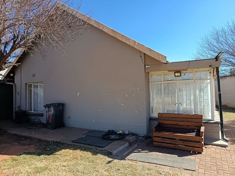 Rear exterior view of the house featuring a paved patio area, security bars on windows, and visible exterior wall paint deterioration.