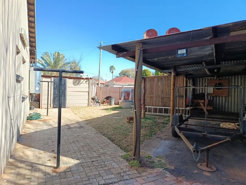Rear yard area featuring a paved walkway, corrugated iron covered structure, and perimeter timber fencing.