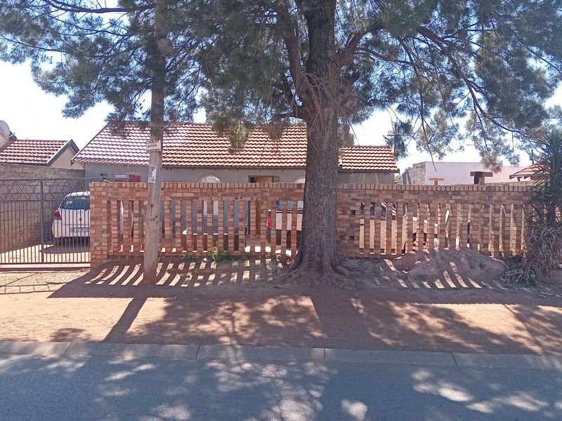 Front view of a residential property featuring a brick boundary wall, metal driveway gate, and a tiled roof structure.