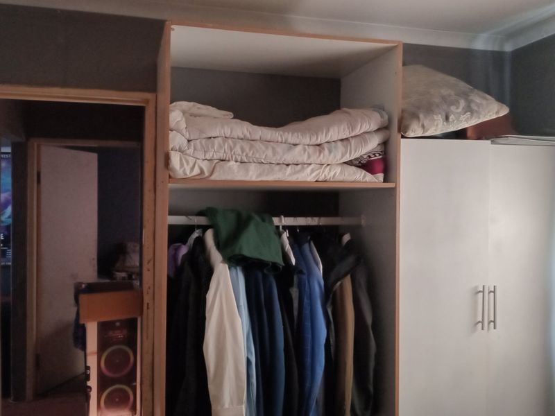 Bedroom featuring a built-in wardrobe with open shelving and hanging space, showing signs of wear and unfinished cabinetry edges.