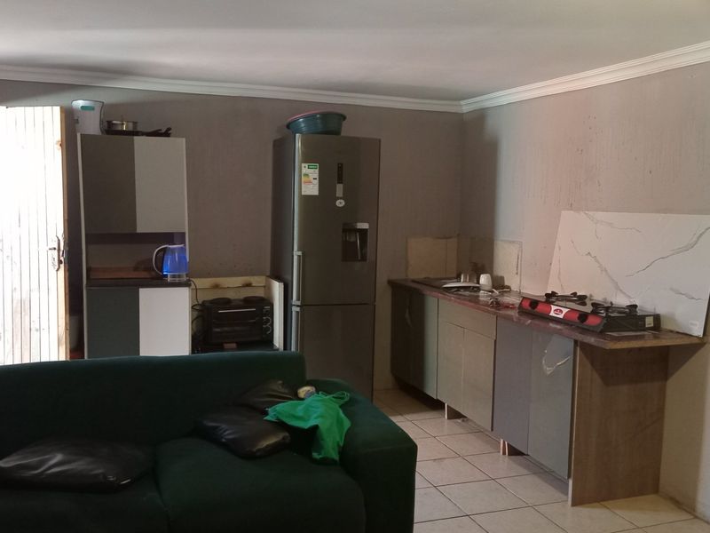 Open plan living and kitchen area featuring tiled floors, basic cabinetry, and unfinished wall surfaces requiring cosmetic attention.