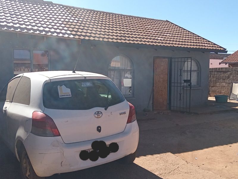 Front elevation of a single-story house featuring a tiled roof, arched windows, and a security gate entrance, set within a walled property boundary.
