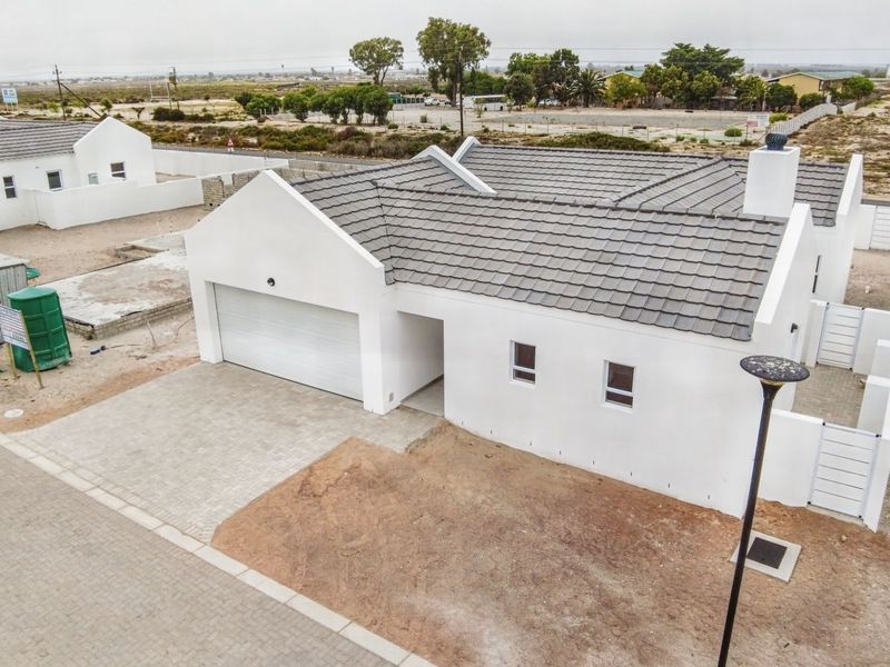 Aerial view of a modern single-story house featuring a tiled roof, attached garage, and paved driveway in a developing residential area.