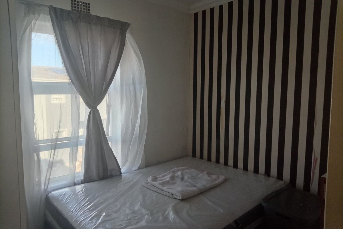 A bedroom featuring a window with curtains and a striped feature wall with visible signs of wear.