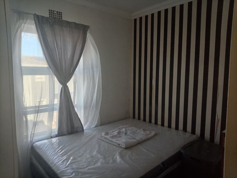 A bedroom featuring a window with curtains and a striped feature wall with visible signs of wear.