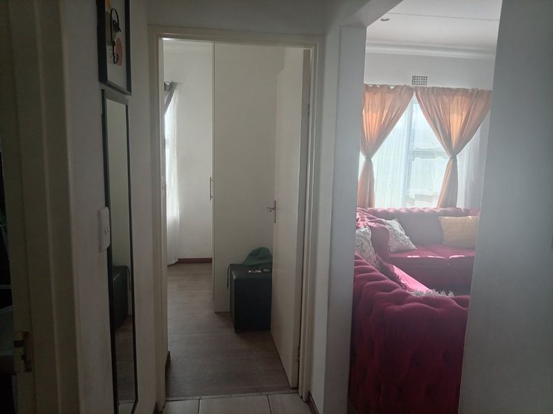 A view from the hallway looking into a living area and an adjacent bedroom featuring built-in cupboards and mixed flooring finishes.