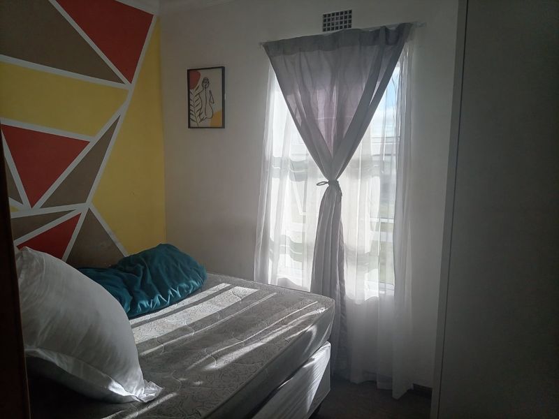 A bedroom featuring a built-in wardrobe and a window with natural light, finished with a decorative geometric wall accent.