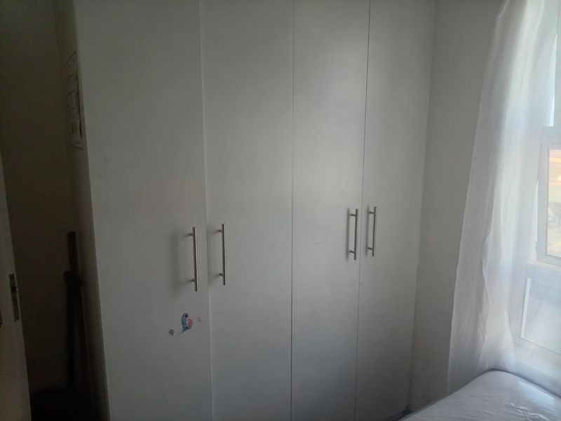 A bedroom featuring white built-in cupboards with modern metal handles and a window allowing natural light into the space.