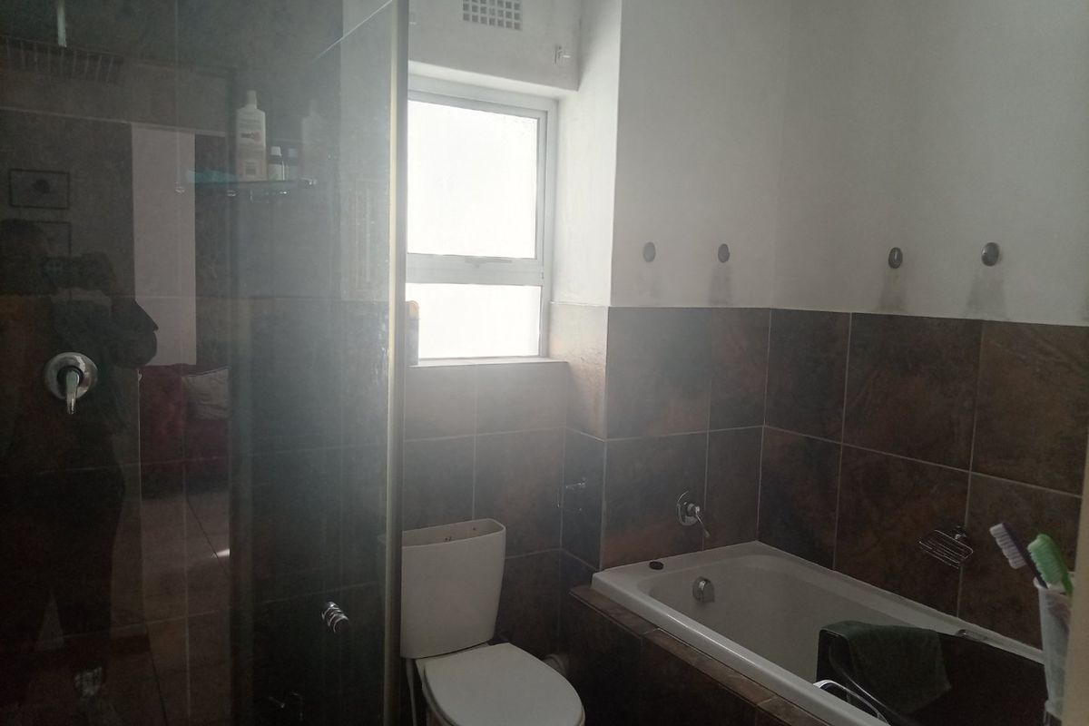 A functional bathroom featuring a built-in bathtub, a glass-enclosed shower, and tiled wall finishes with a window for natural light.