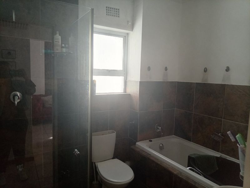 A functional bathroom featuring a built-in bathtub, a glass-enclosed shower, and tiled wall finishes with a window for natural light.
