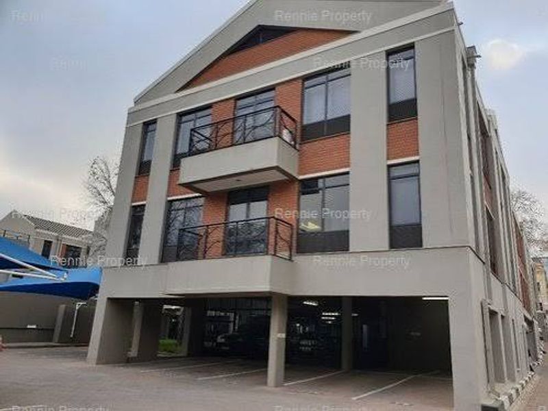 A multi-story commercial building featuring a brick and plaster facade, private balconies with wrought iron railings, and ground-level covered parking bays.