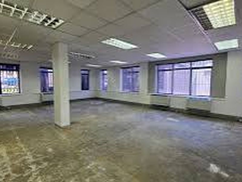 An open-plan commercial office space featuring suspended ceilings, fluorescent lighting, security bars on windows, and exposed concrete flooring.