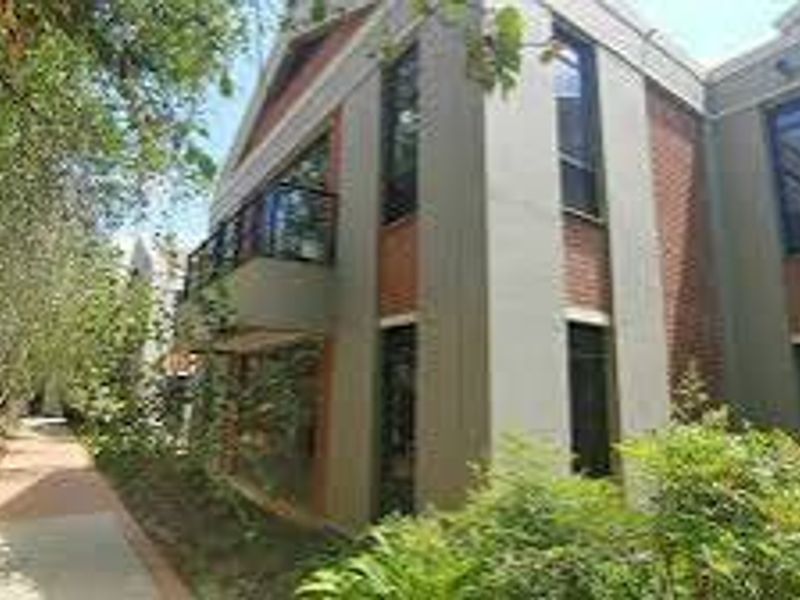 A view of the rear exterior of the commercial building, featuring a brick facade, a balcony, and a paved walkway through the garden.
