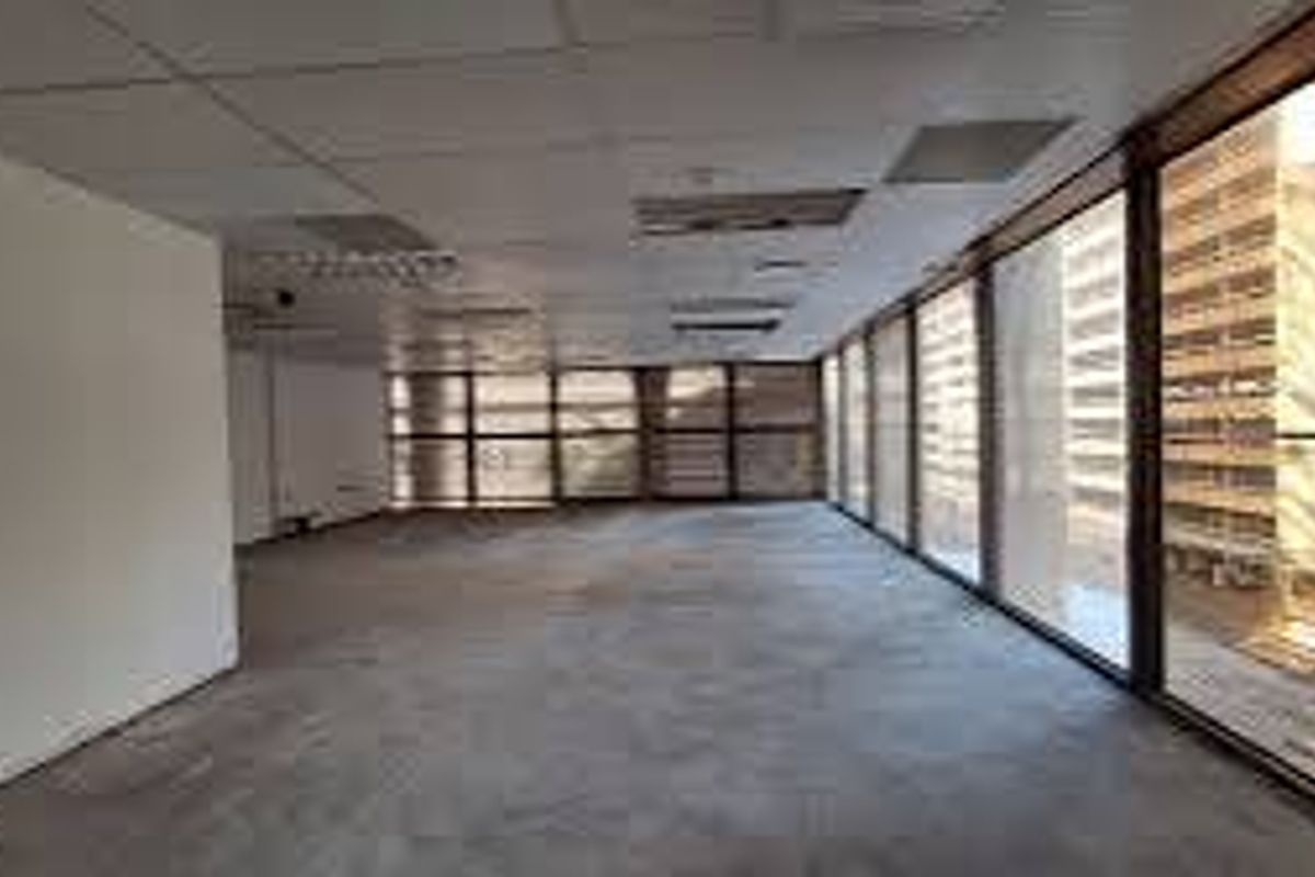 An empty, open-plan commercial office space featuring large windows with city views, a suspended ceiling, and carpeted flooring.