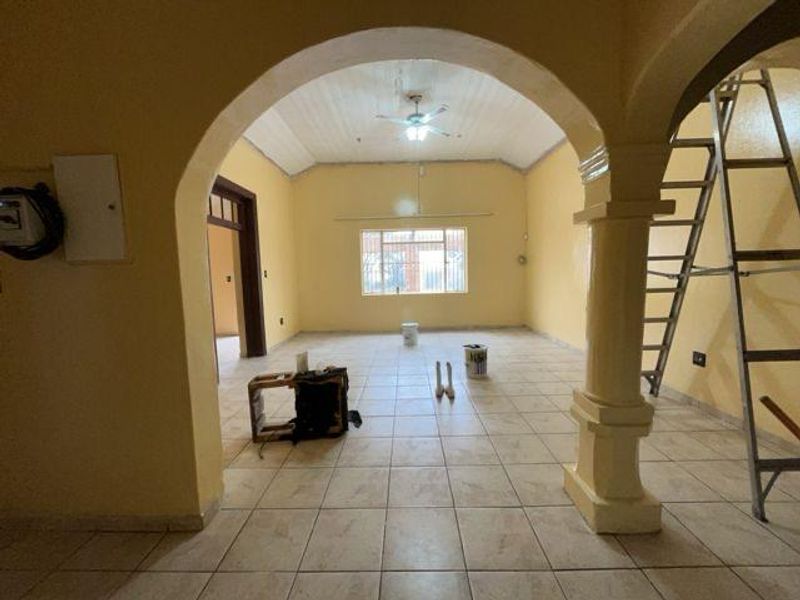 Spacious living area featuring an arched entryway, vaulted ceilings with a fan, and tiled flooring, currently undergoing maintenance and ready for renovation.