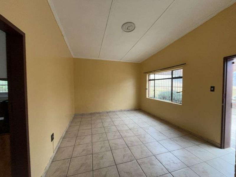An empty living room featuring tiled flooring, a window with security bars, and neutral wall paint, offering a blank canvas for interior design.