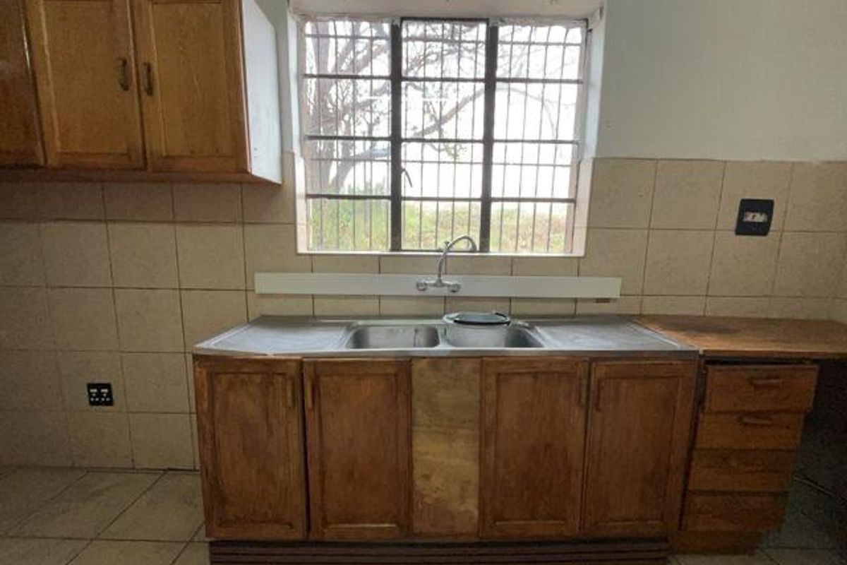 A dated kitchen area featuring wooden cabinetry, a double basin sink, tiled backsplash, and security bars on the window.