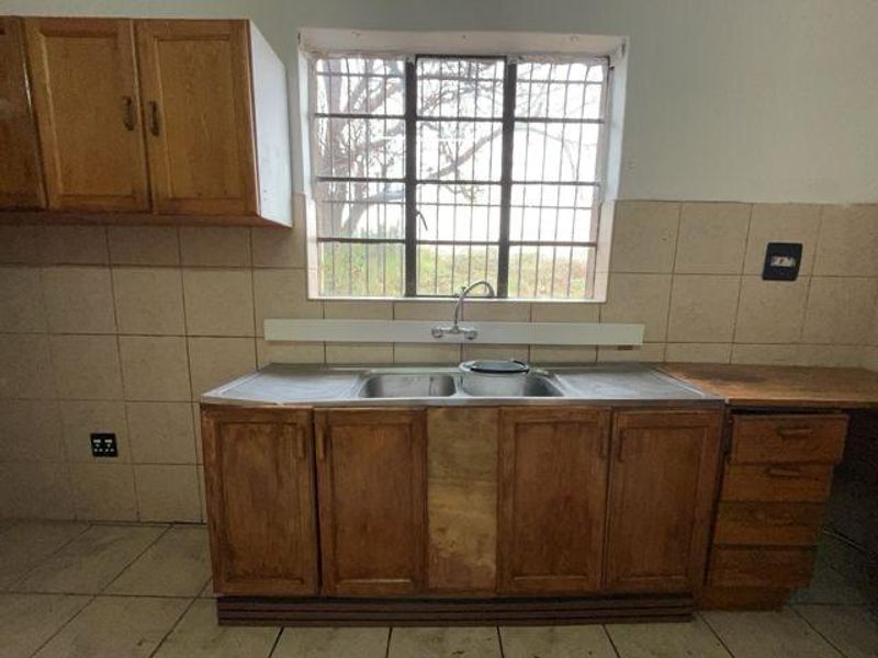 A dated kitchen area featuring wooden cabinetry, a double basin sink, tiled backsplash, and security bars on the window.