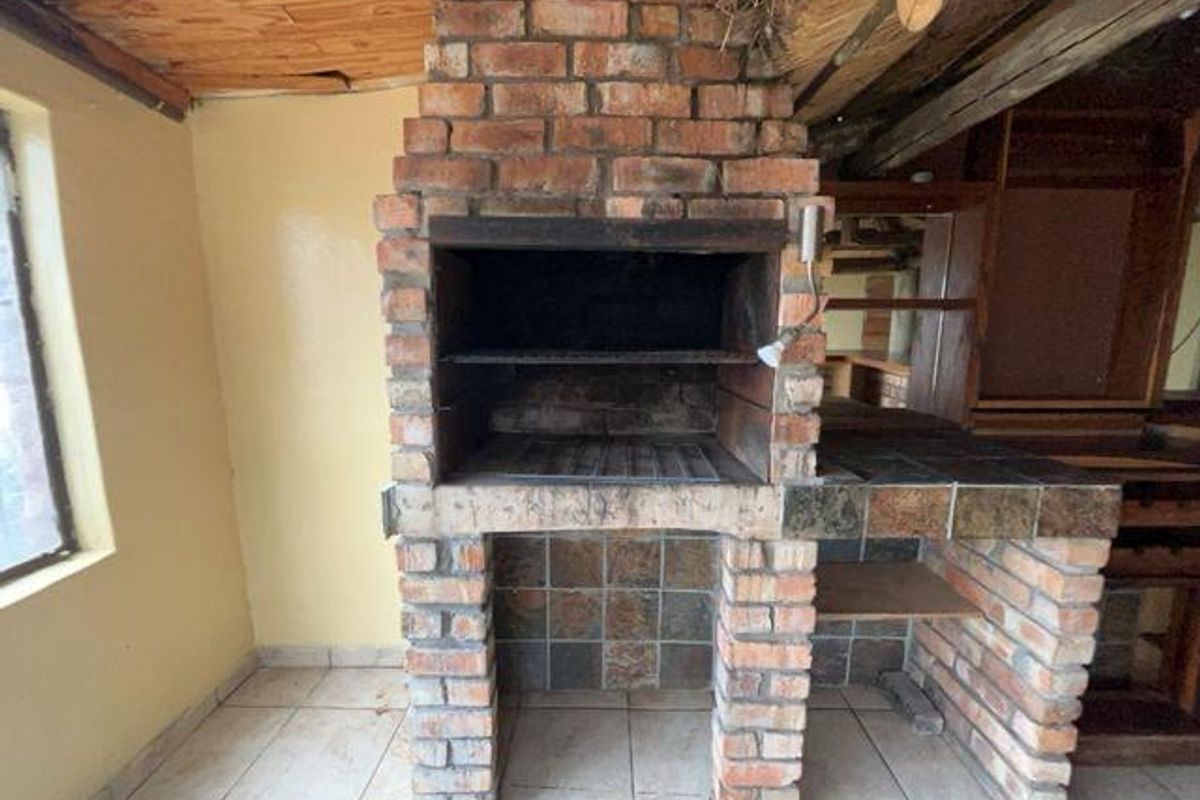 An indoor entertainment area featuring a large built-in brick braai, tiled prep counter, and rustic exposed timber ceiling.