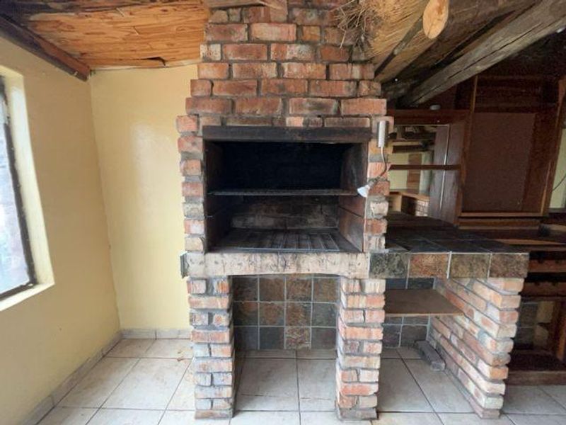 An indoor entertainment area featuring a large built-in brick braai, tiled prep counter, and rustic exposed timber ceiling.