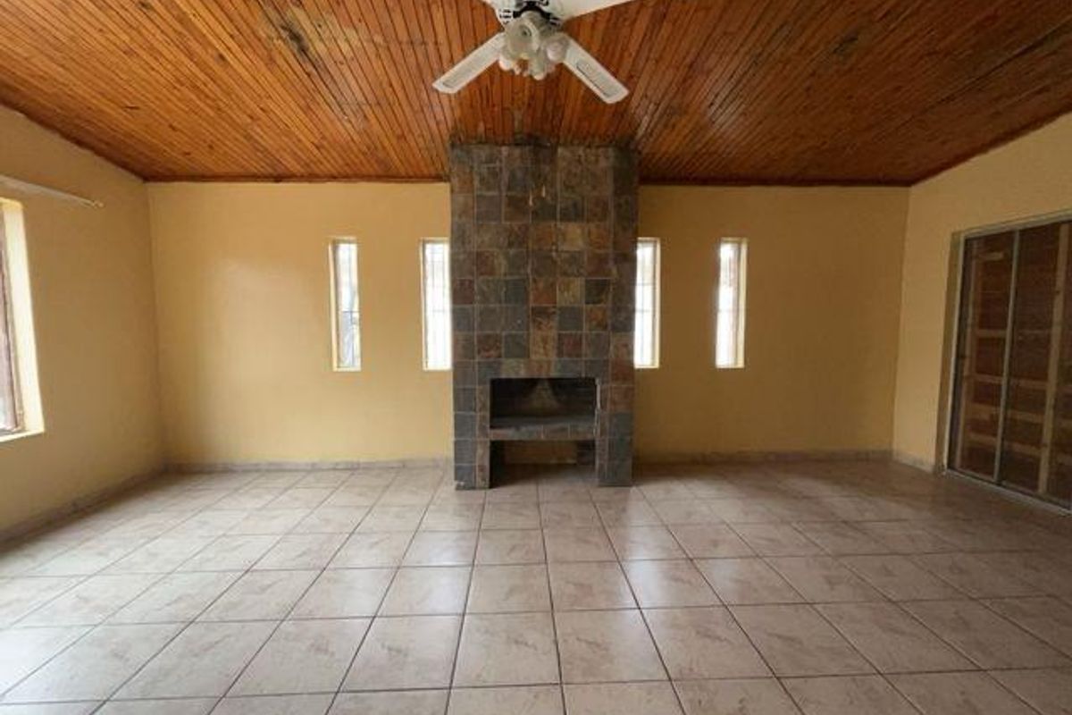 Spacious living area featuring a central stone-clad fireplace, tiled flooring, and a timber-paneled ceiling with an integrated fan.