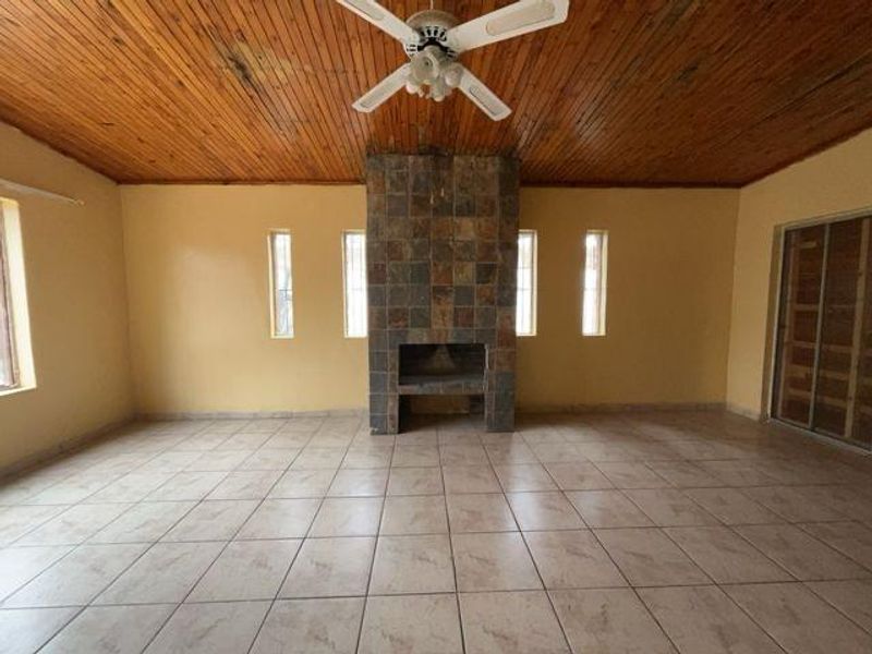 Spacious living area featuring a central stone-clad fireplace, tiled flooring, and a timber-paneled ceiling with an integrated fan.