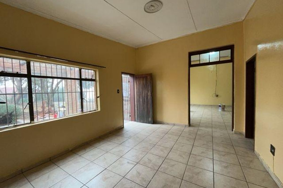 An empty, neutrally painted living area featuring tiled flooring, security bars on the windows, and direct access to adjacent rooms.