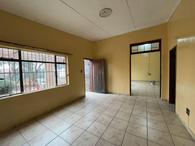 An empty, neutrally painted living area featuring tiled flooring, security bars on the windows, and direct access to adjacent rooms.