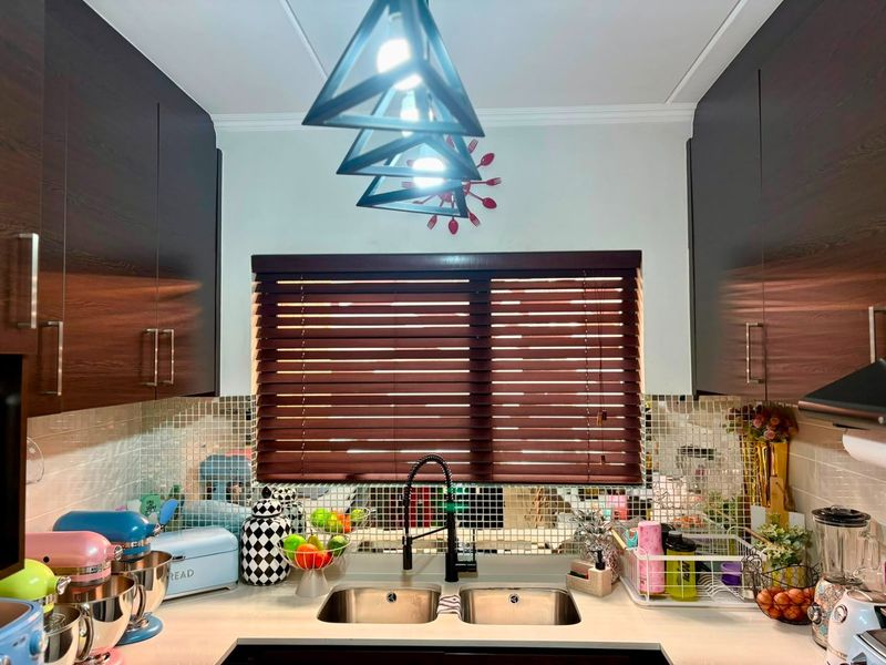 A compact kitchen featuring dark wood cabinetry, a mosaic tile backsplash, and a double stainless steel sink with a modern gooseneck faucet.