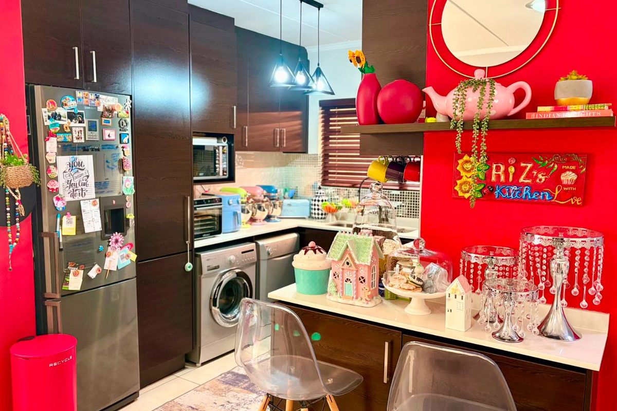 A compact kitchen featuring dark wood cabinetry, stone countertops, integrated appliances, and a breakfast bar area with vibrant red accent walls.