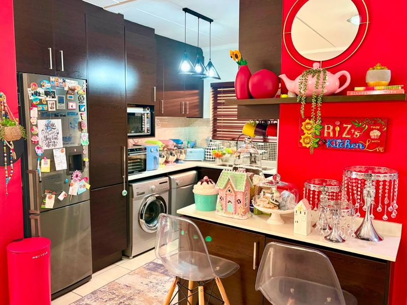 A compact kitchen featuring dark wood cabinetry, stone countertops, integrated appliances, and a breakfast bar area with vibrant red accent walls.