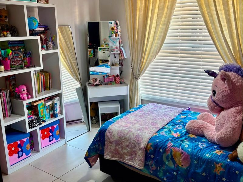 A well-maintained bedroom featuring neutral tiled flooring, venetian blinds, and soft window treatments, providing a comfortable and functional living space.