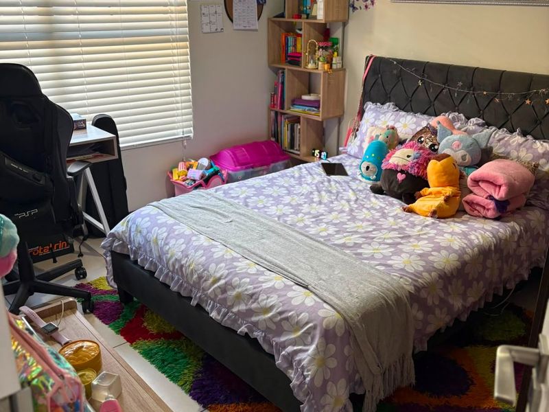 A well-maintained bedroom featuring tiled flooring, venetian blinds, and a wall-mounted mirror, providing a functional and comfortable living space.