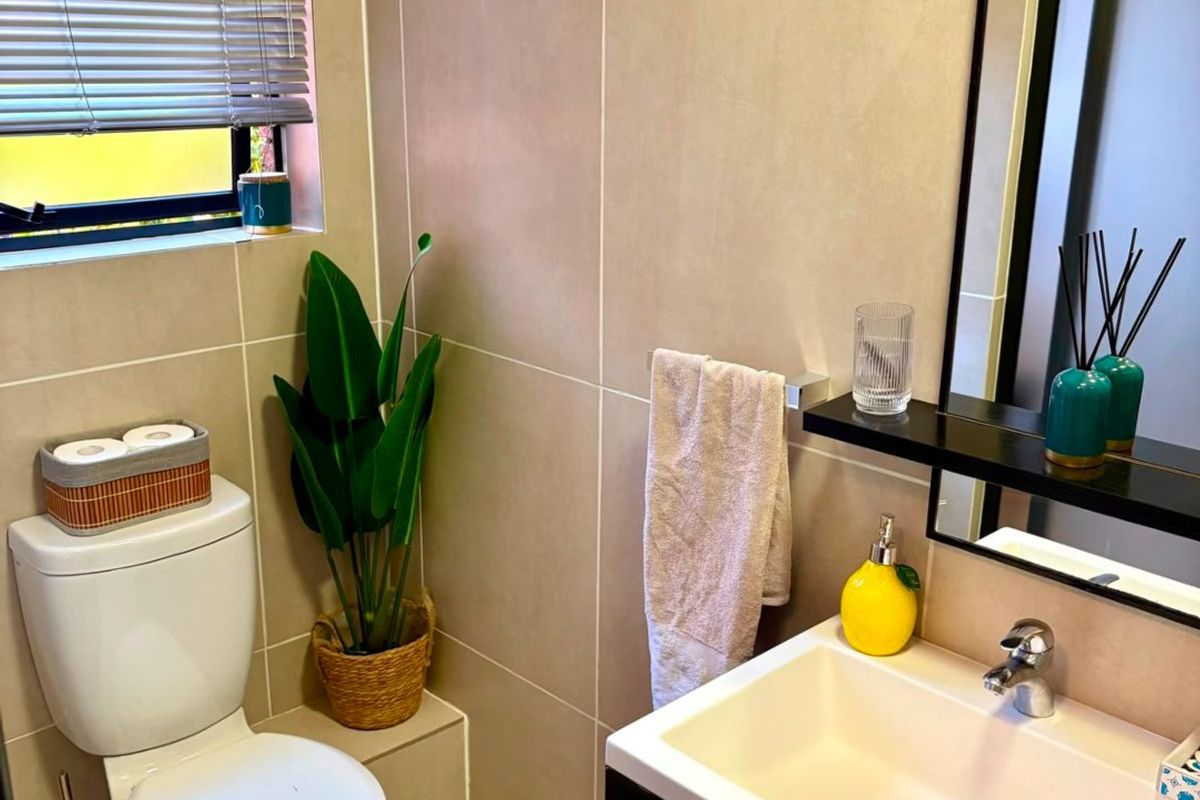 A modern, well-maintained bathroom featuring neutral wall and floor tiling, a contemporary vanity with basin, and a window with fitted venetian blinds.