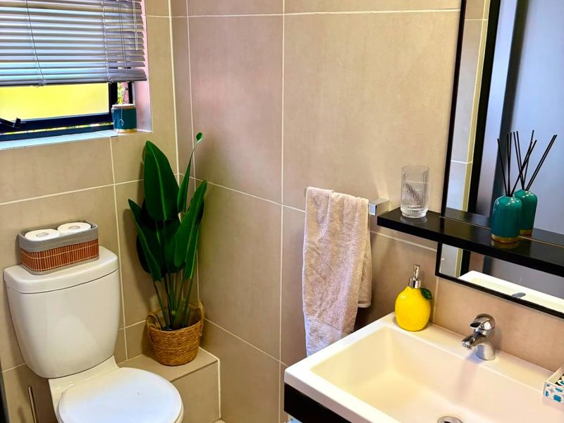 A modern, well-maintained bathroom featuring neutral wall and floor tiling, a contemporary vanity with basin, and a window with fitted venetian blinds.