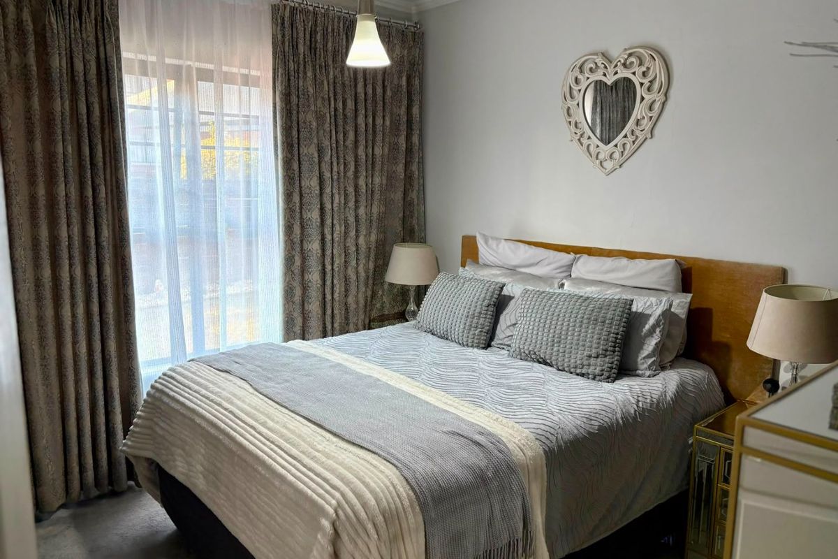 A well-maintained bedroom featuring neutral wall finishes, a ceiling pendant light, and a sliding glass door with floor-to-ceiling curtains.