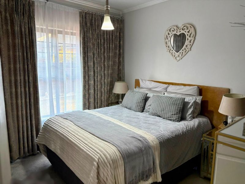 A well-maintained bedroom featuring neutral wall finishes, a ceiling pendant light, and a sliding glass door with floor-to-ceiling curtains.