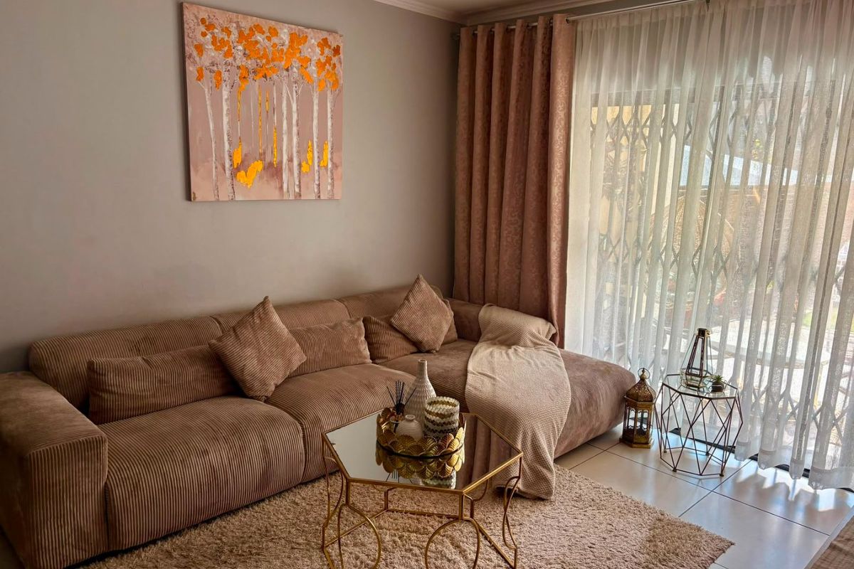 A well-maintained living room featuring tiled flooring and a large sliding glass door with security gate, providing access to the outdoor area.