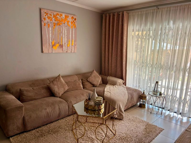 A well-maintained living room featuring tiled flooring and a large sliding glass door with security gate, providing access to the outdoor area.