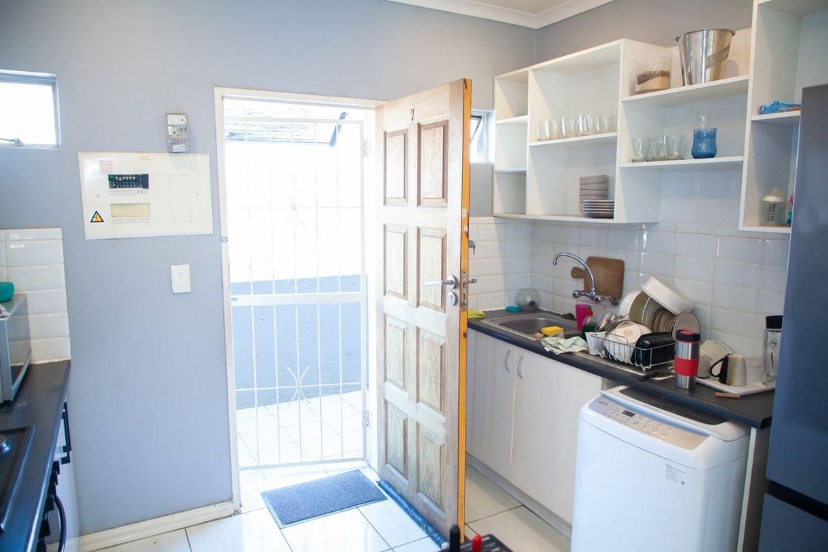 A functional kitchen area featuring built-in cabinetry, tiled backsplash, and direct access to an exterior space through a security gate.