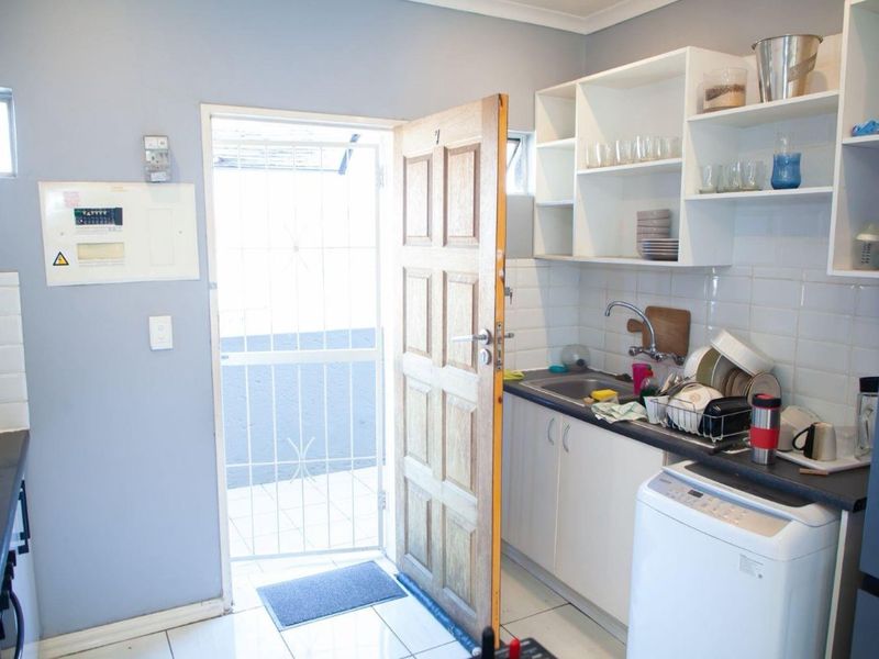 A functional kitchen area featuring built-in cabinetry, tiled backsplash, and direct access to an exterior space through a security gate.