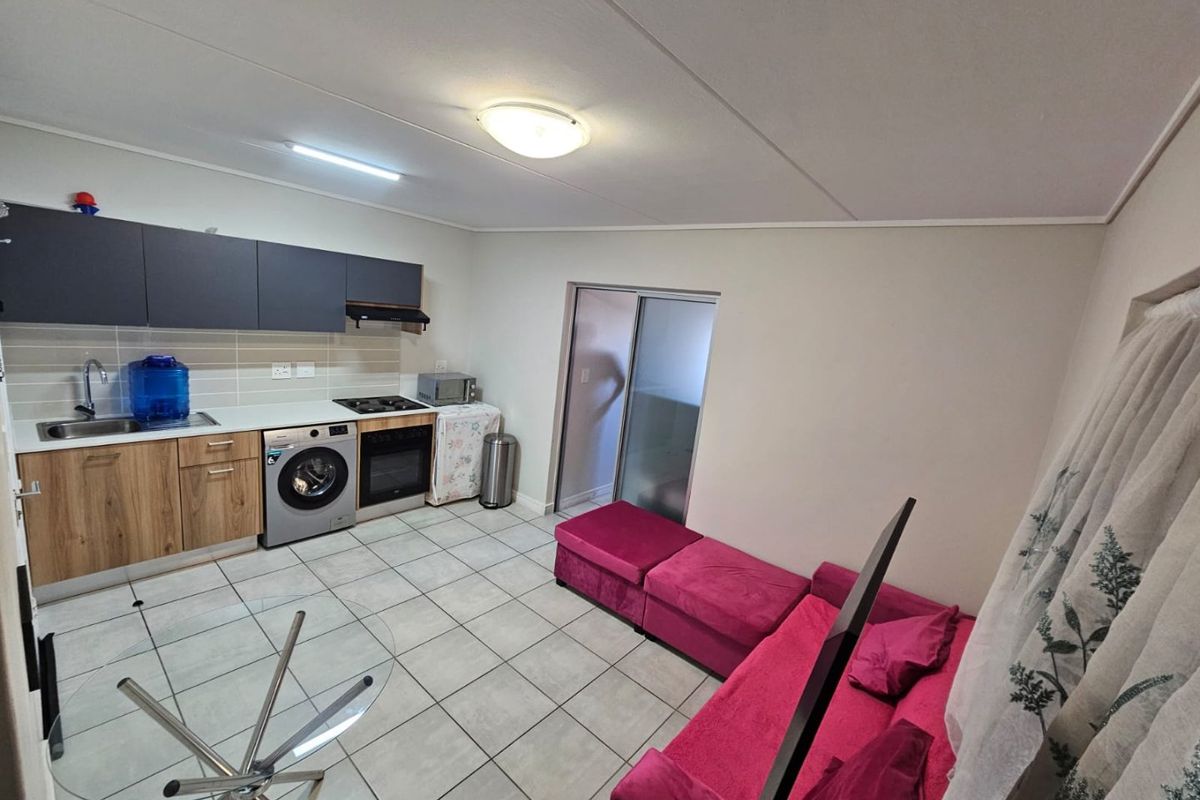 Open-plan living area featuring a compact kitchen with built-in cabinetry, oven, hob, and tiled flooring, leading to a sliding door.
