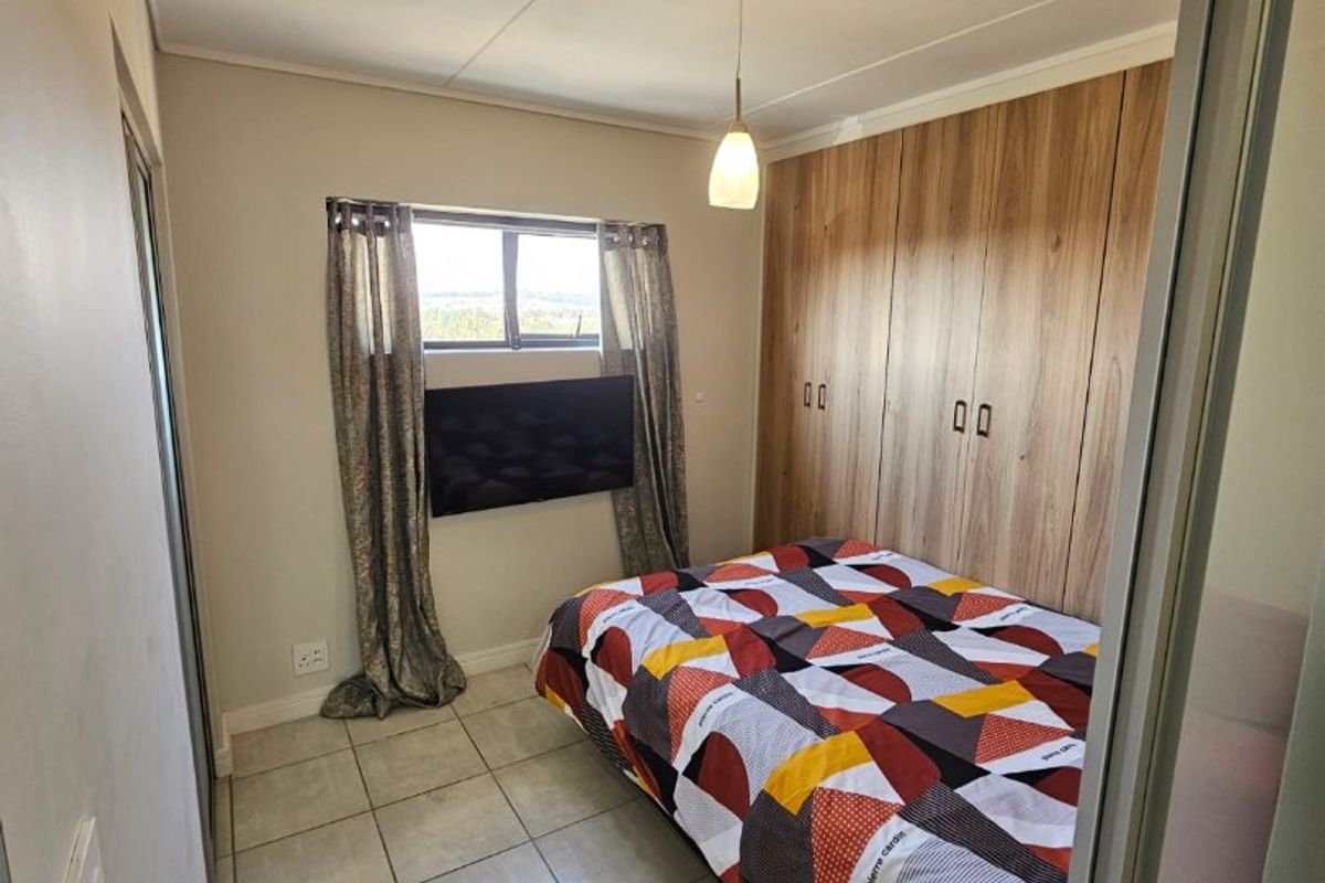 A compact bedroom featuring built-in wooden cupboards, tiled flooring, and a window providing natural light.